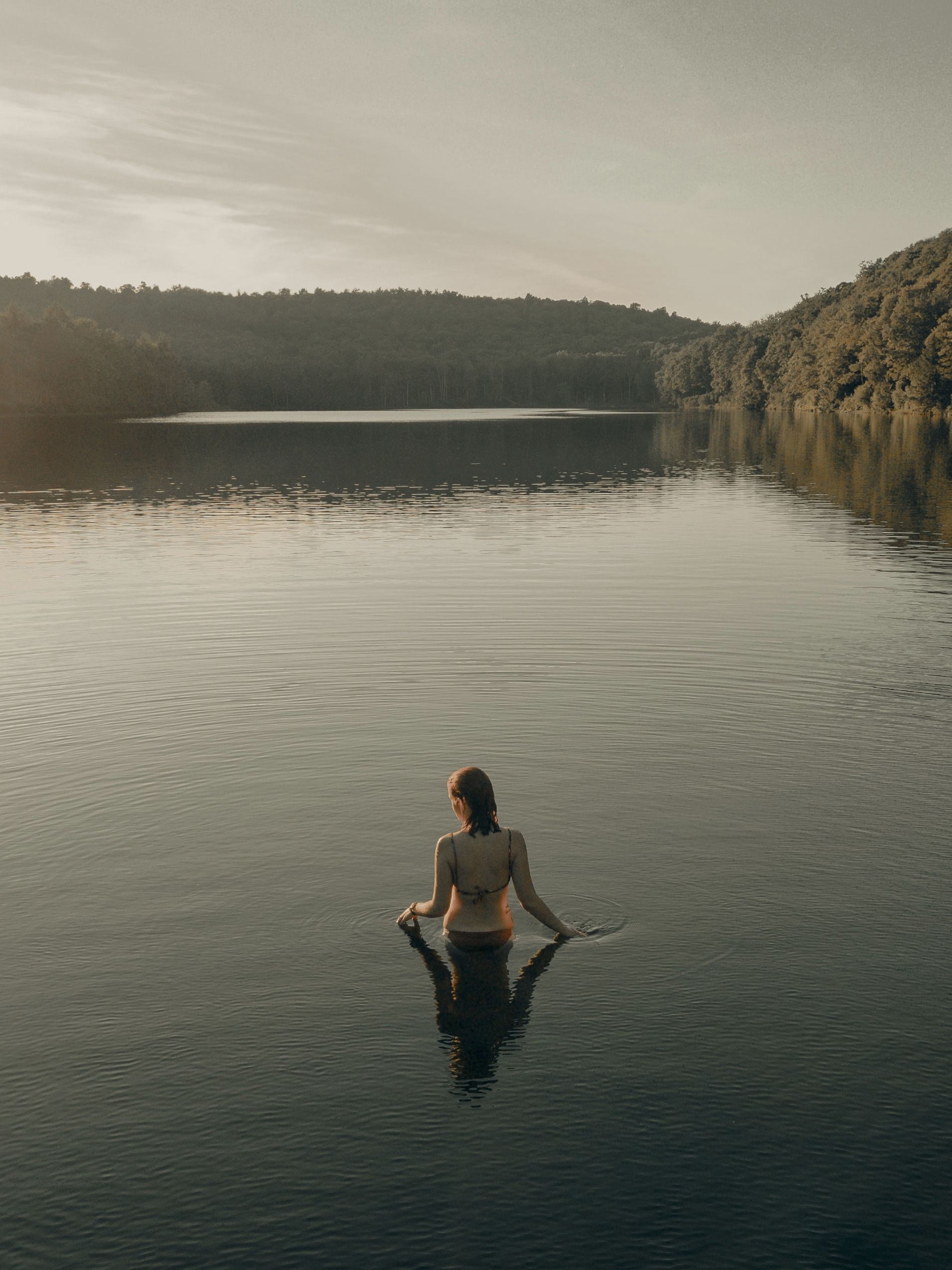 woman in black bikini sitting on rock near body of water during daytime